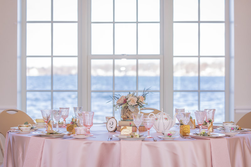 Pink bridal shower dish rentals on table in front of a white window with a view of the lake at the main beach venue in Crystal Lake Il