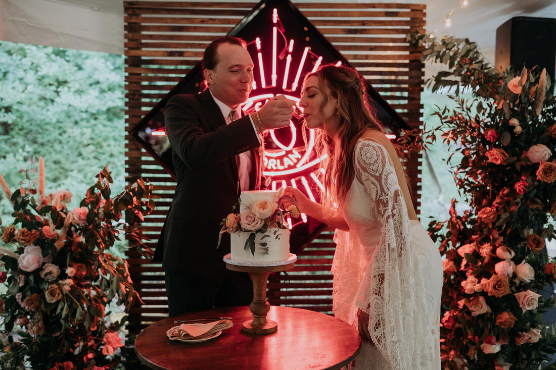 Bride and groom cutting the cake in front of a neon sign