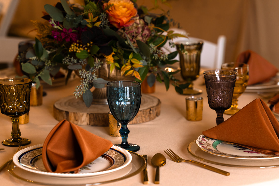 Hammered glass charger, Bold and Beautiful dinnerware, multi-colored goblets, brushed gold flatware and linen rentals