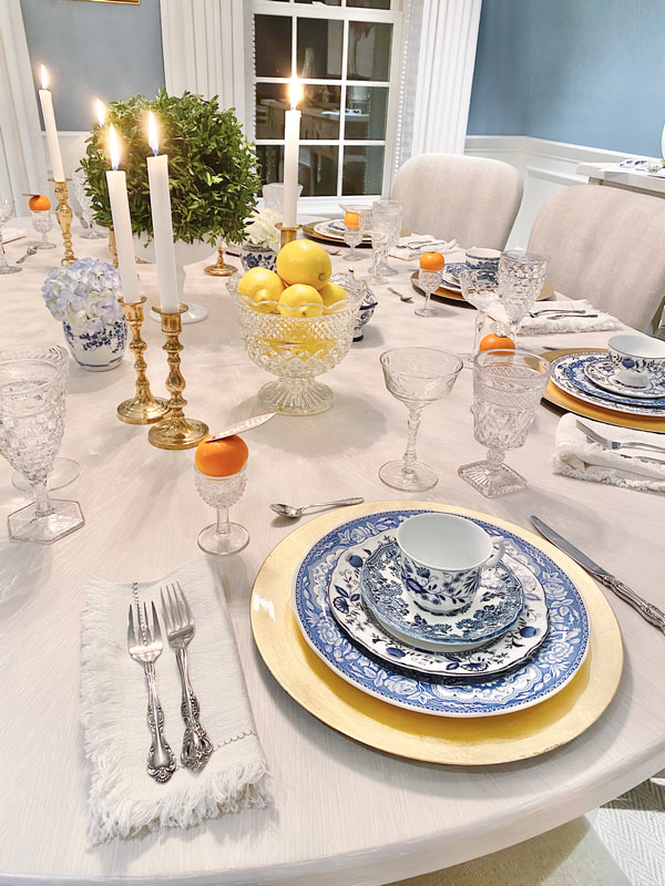 A table setting with Blue and white dinnerware rentals with cutie oranges sitting on top of stemmed shot glasses with a leaf pinned to the orange as a name card. Crystal bowl filled with lemons in Winnetka IL  